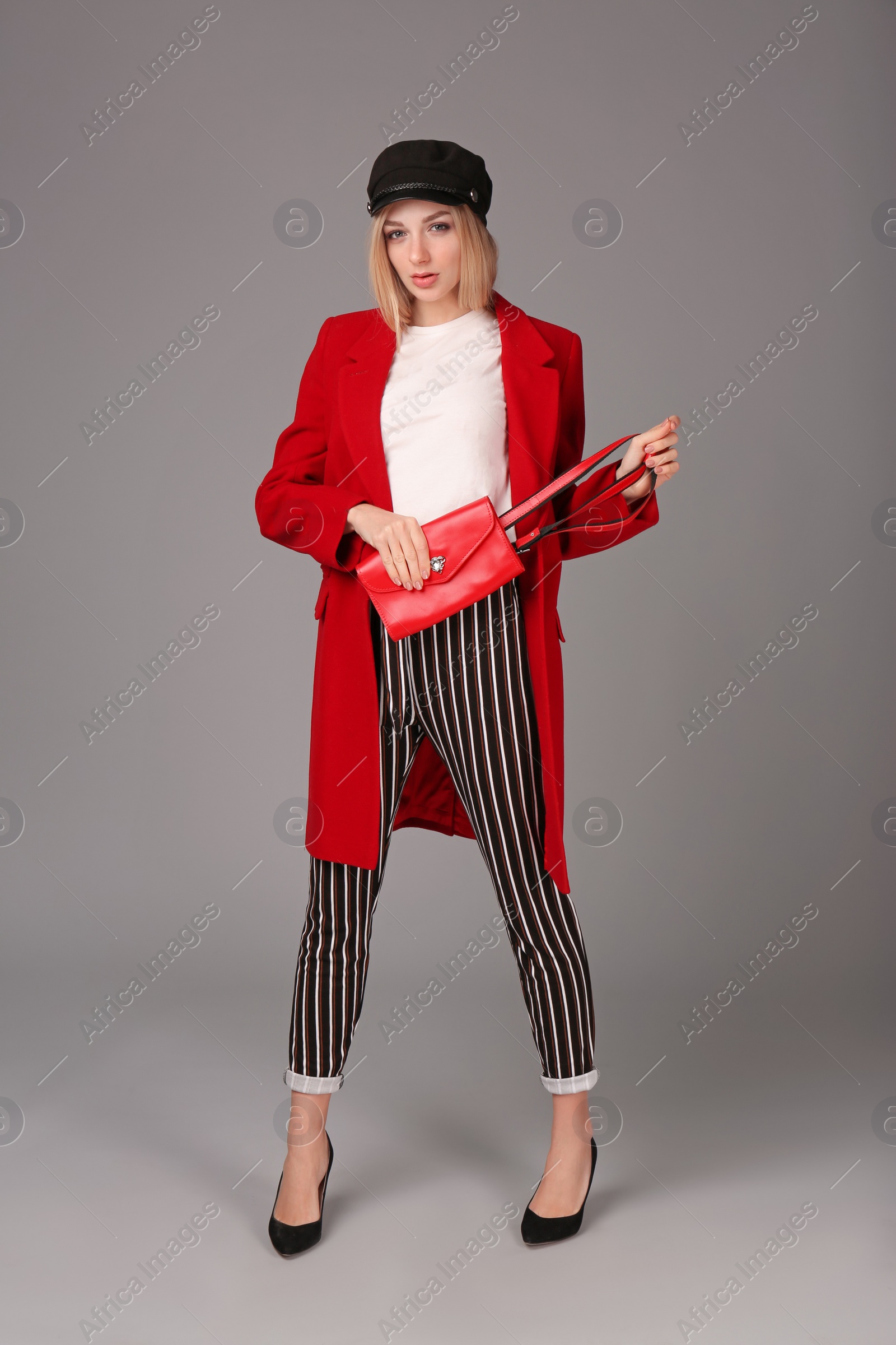 Photo of Young stylish woman in trendy shoes with bum bag on grey background