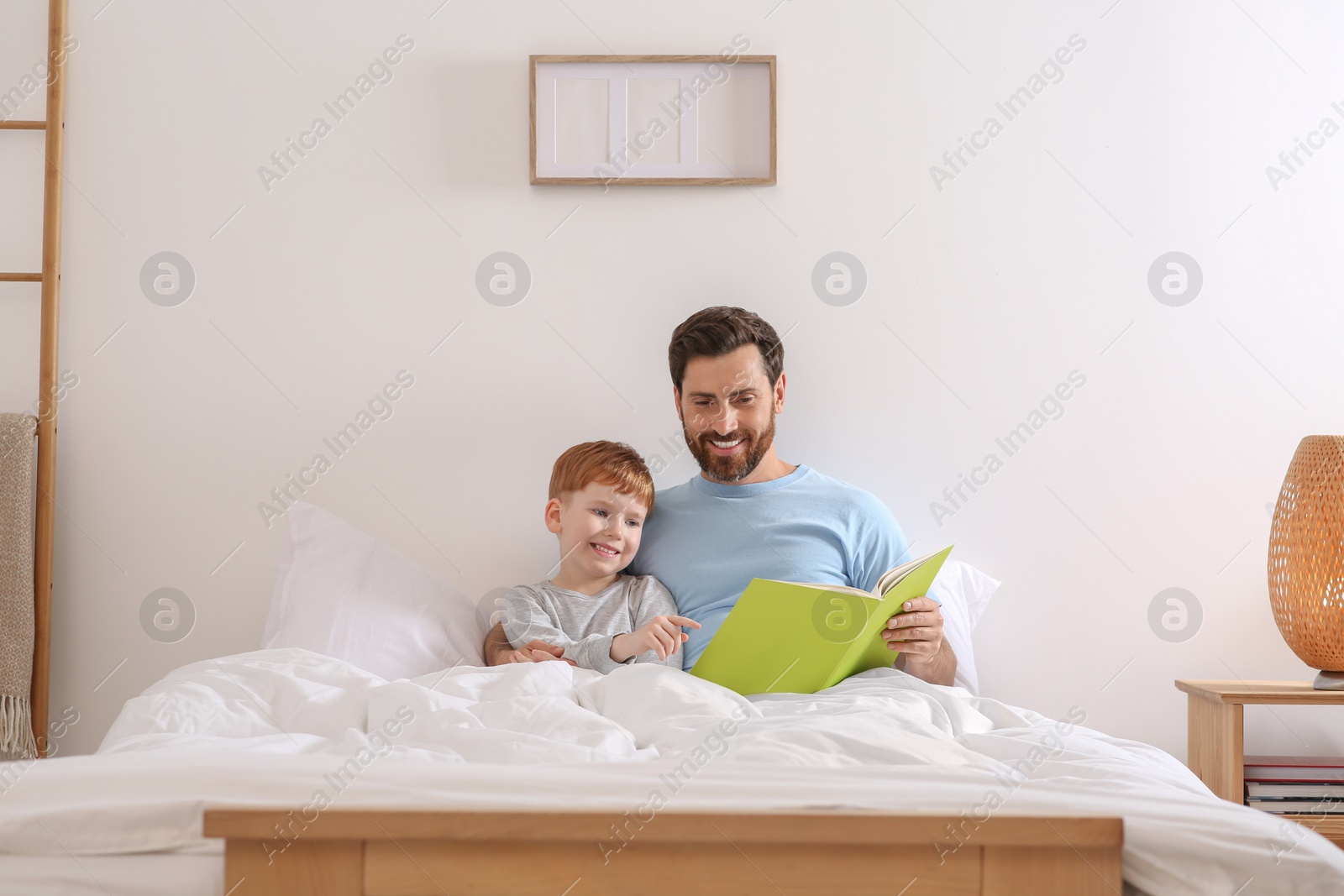 Photo of Father reading book with his child on bed at home