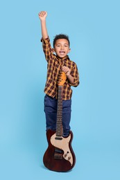 Cute African-American boy with electric guitar on turquoise background