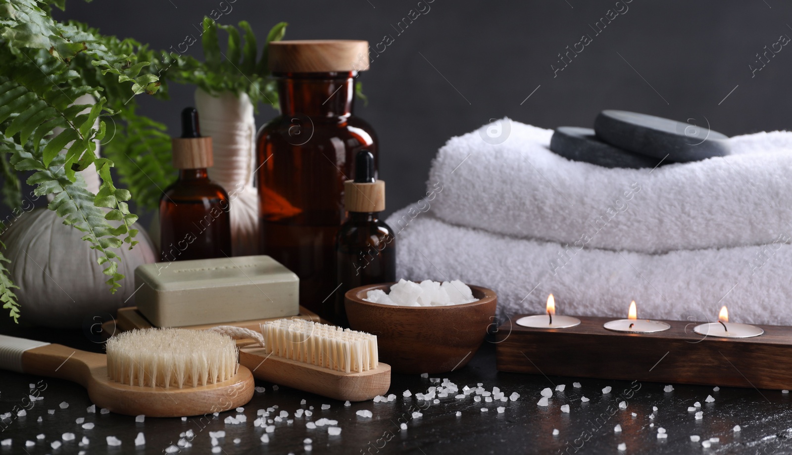 Photo of Spa composition. Brushes, soap bar, sea salt and burning candles on black table