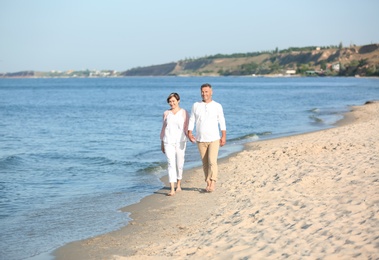 Happy mature couple walking at beach on sunny day