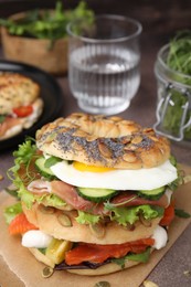 Tasty bagel with cured ham, egg, salmon and vegetables on brown table, closeup