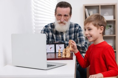 Grandfather and grandson playing chess following online lesson in room