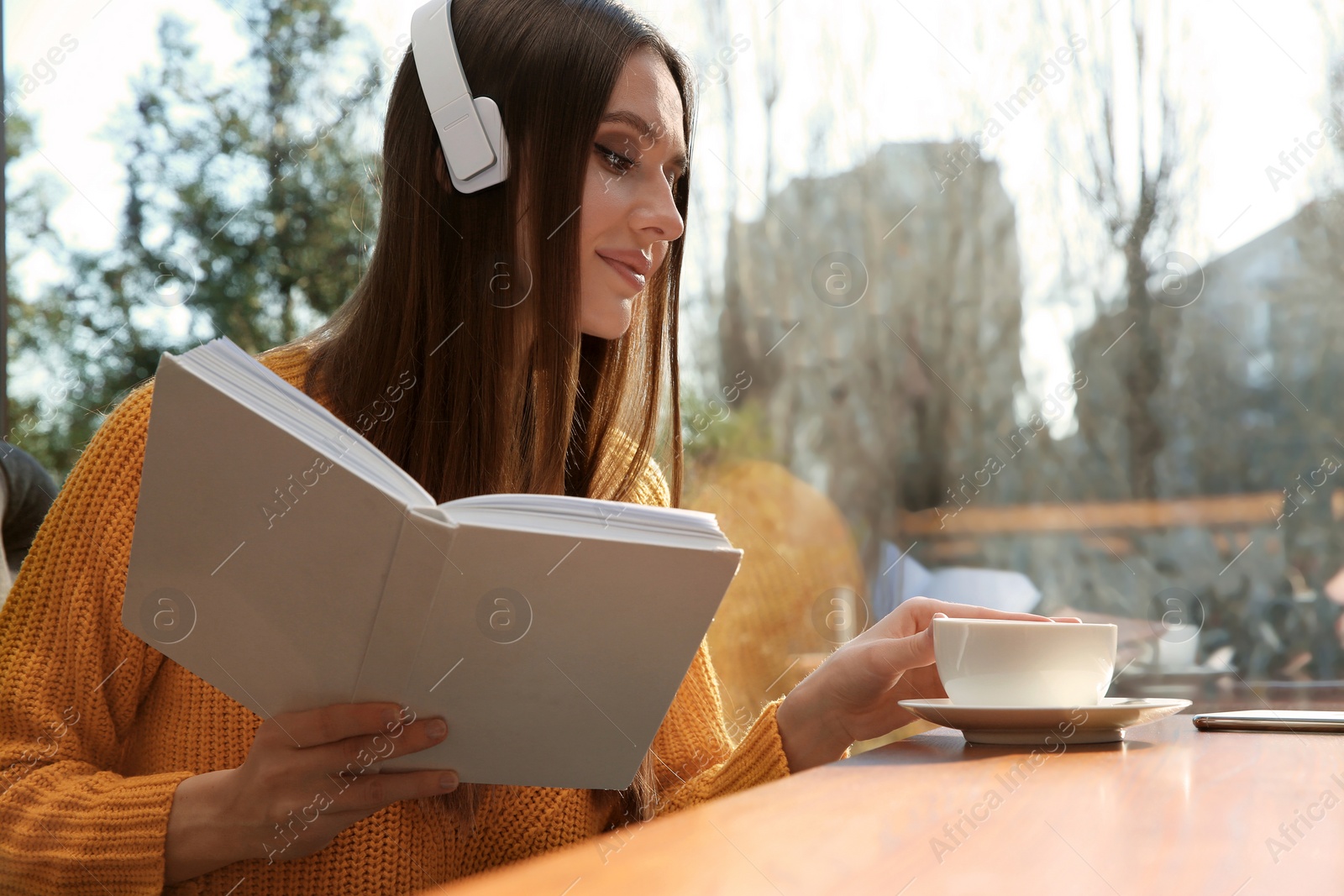 Photo of Woman listening to audiobook at table in cafe