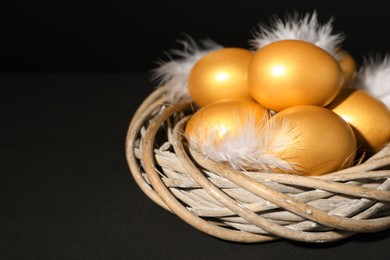 Photo of Shiny golden eggs with feathers in nest on black background, closeup. Space for text