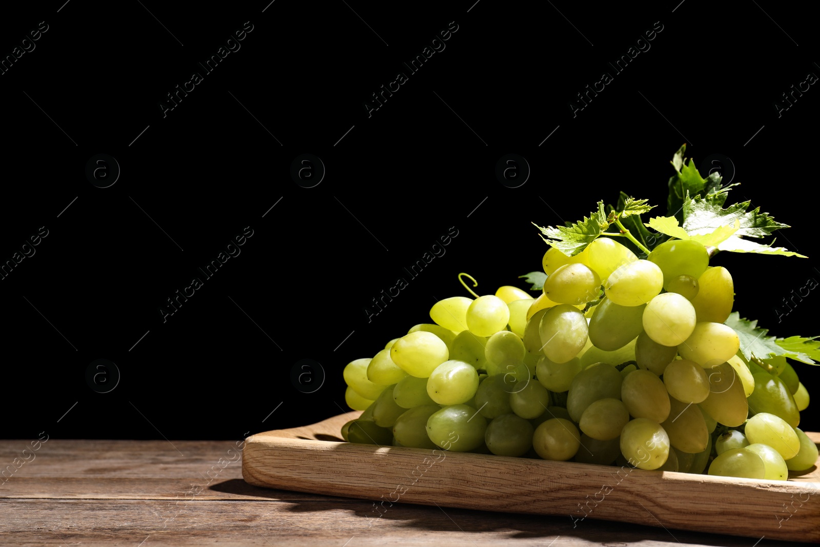 Photo of Fresh ripe juicy grapes on wooden table against black background, space for text