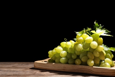 Fresh ripe juicy grapes on wooden table against black background, space for text