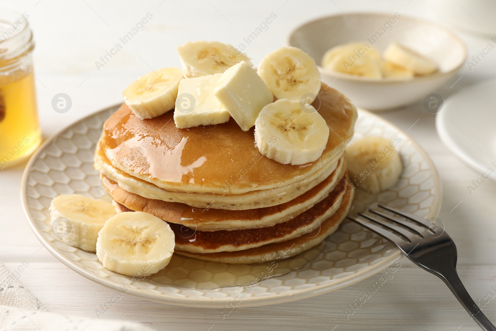 Photo of Delicious pancakes with bananas, honey and butter on white wooden table, closeup