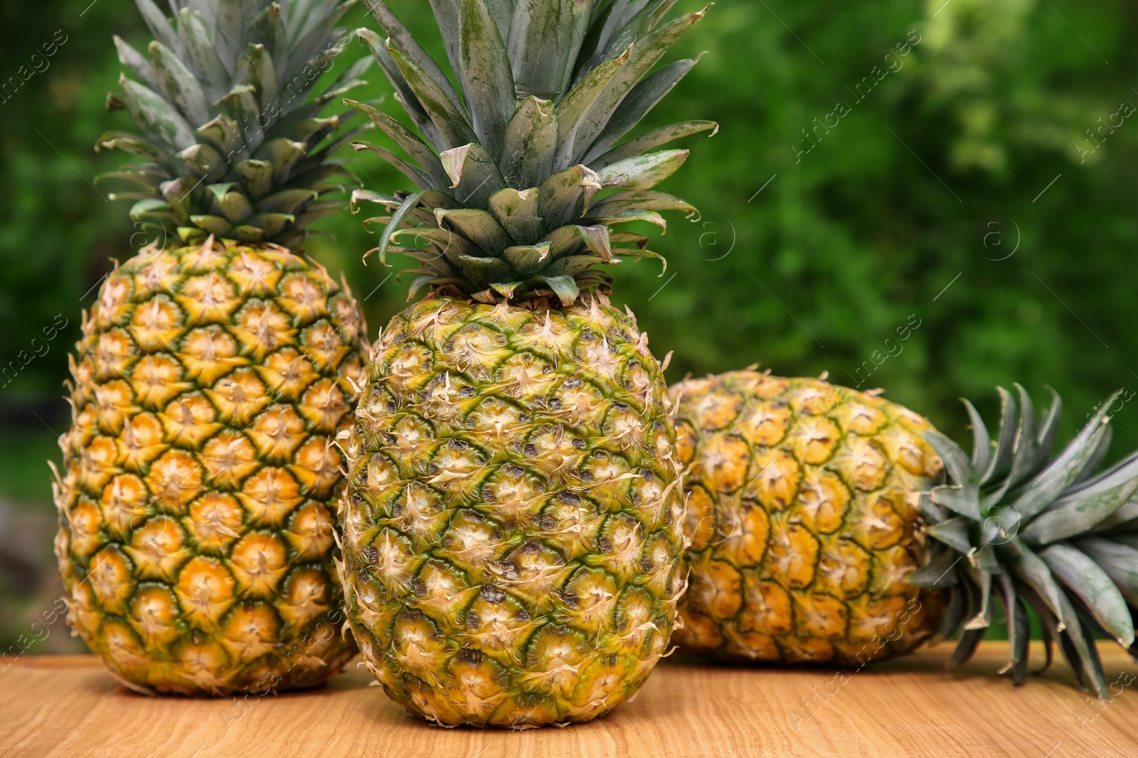 Photo of Delicious ripe pineapples on wooden table outdoors