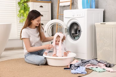 Happy mother with her daughter having fun while washing baby clothes in bathroom