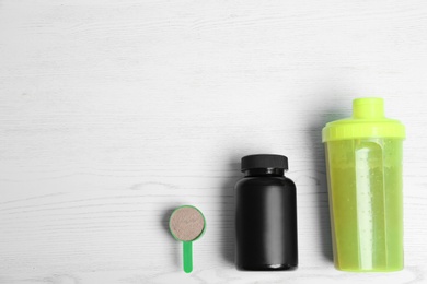 Photo of Bottle of protein shake, jar and scoop with powder on white wooden background, top view. Space for text