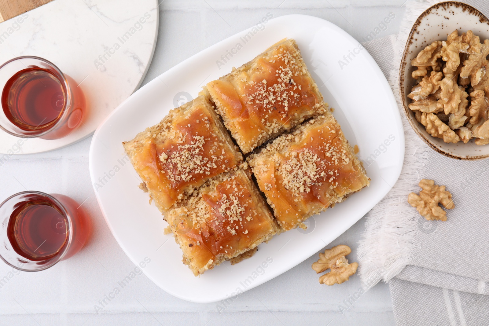 Photo of Eastern sweets. Pieces of tasty baklava, walnuts and tea on white tiled table, flat lay