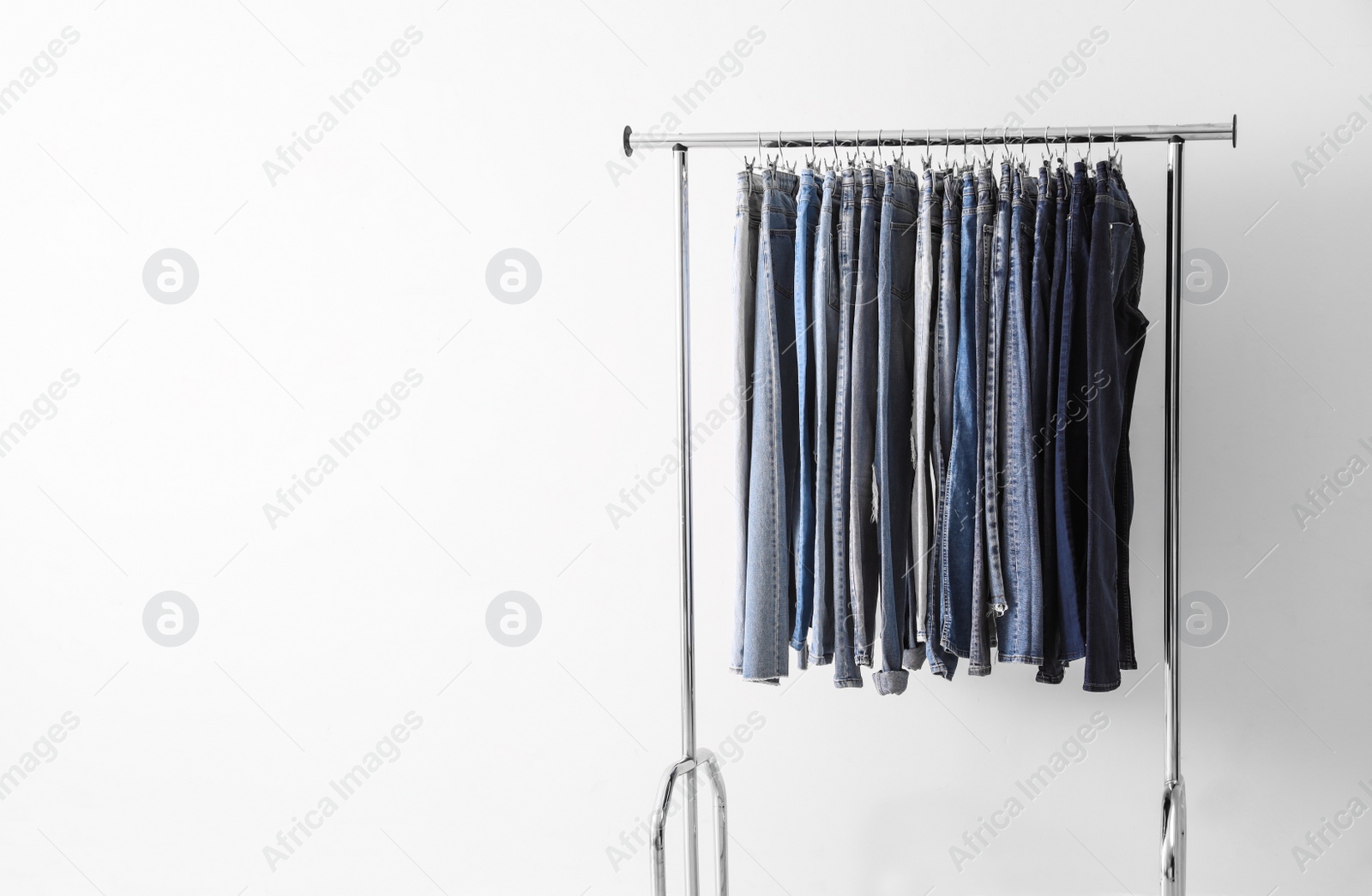 Photo of Rack with different jeans near light wall. Space for text