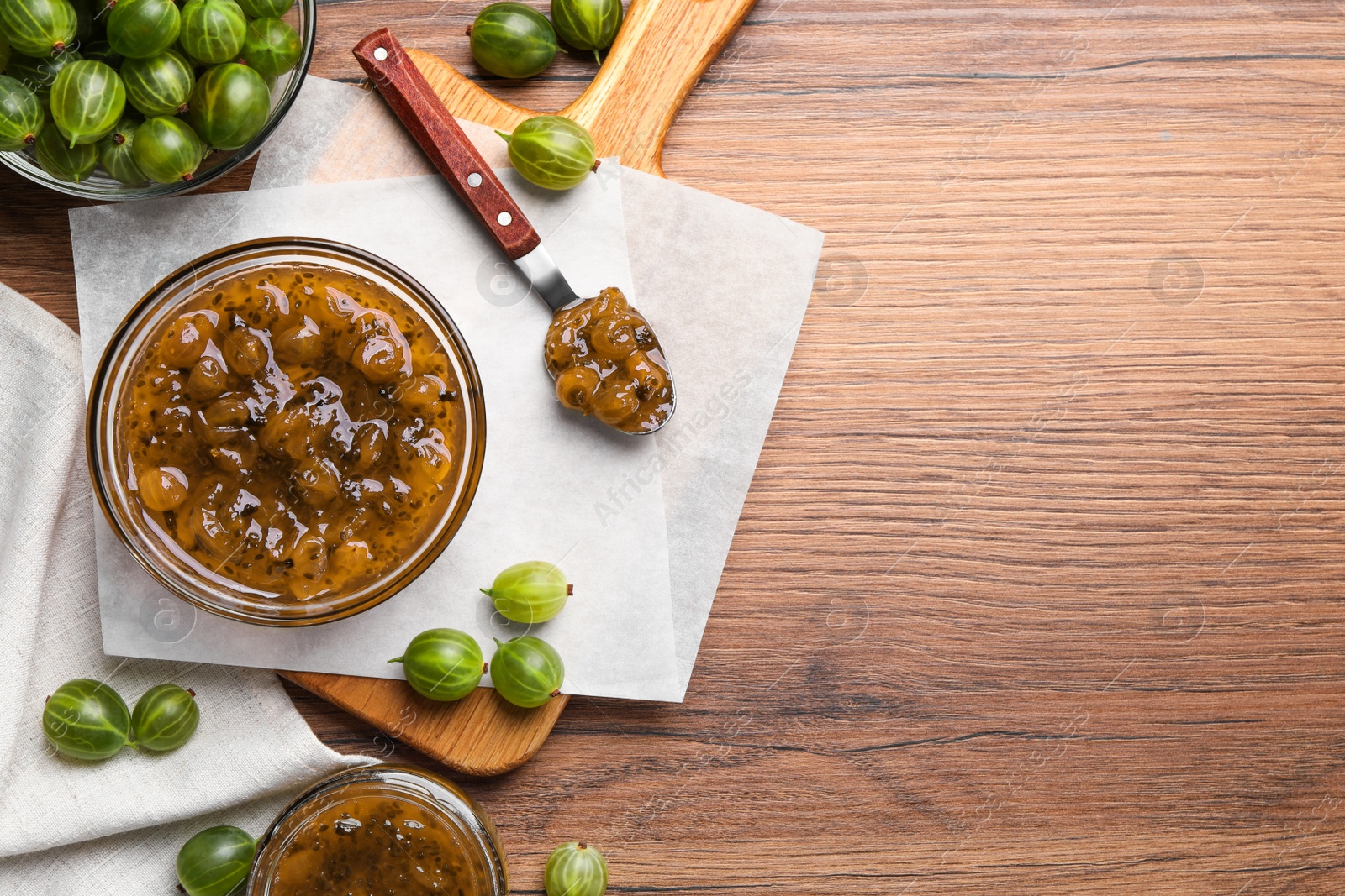 Photo of Bowl, jar, spoon of delicious gooseberry jam and fresh berries on wooden table, flat lay. Space for text