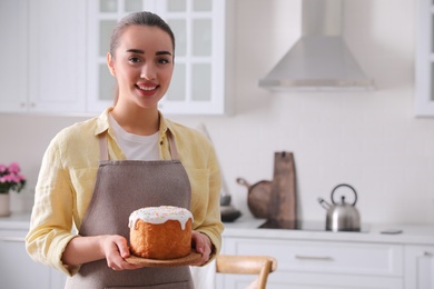 Photo of Young woman with traditional Easter cake in kitchen, space for text