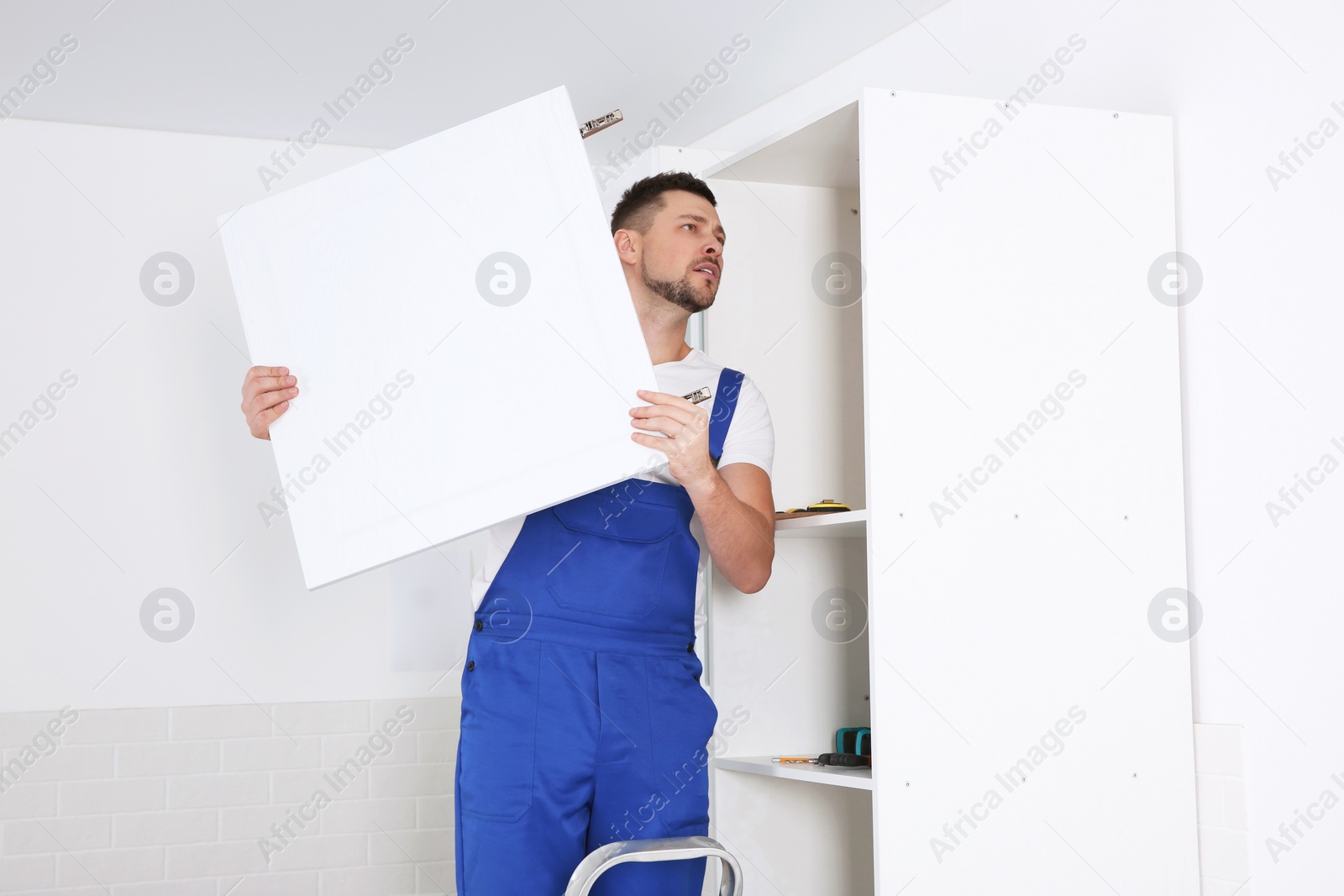 Photo of Worker installing door of cabinet in kitchen