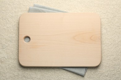 Wooden cutting board and napkin on beige table, top view. Space for text