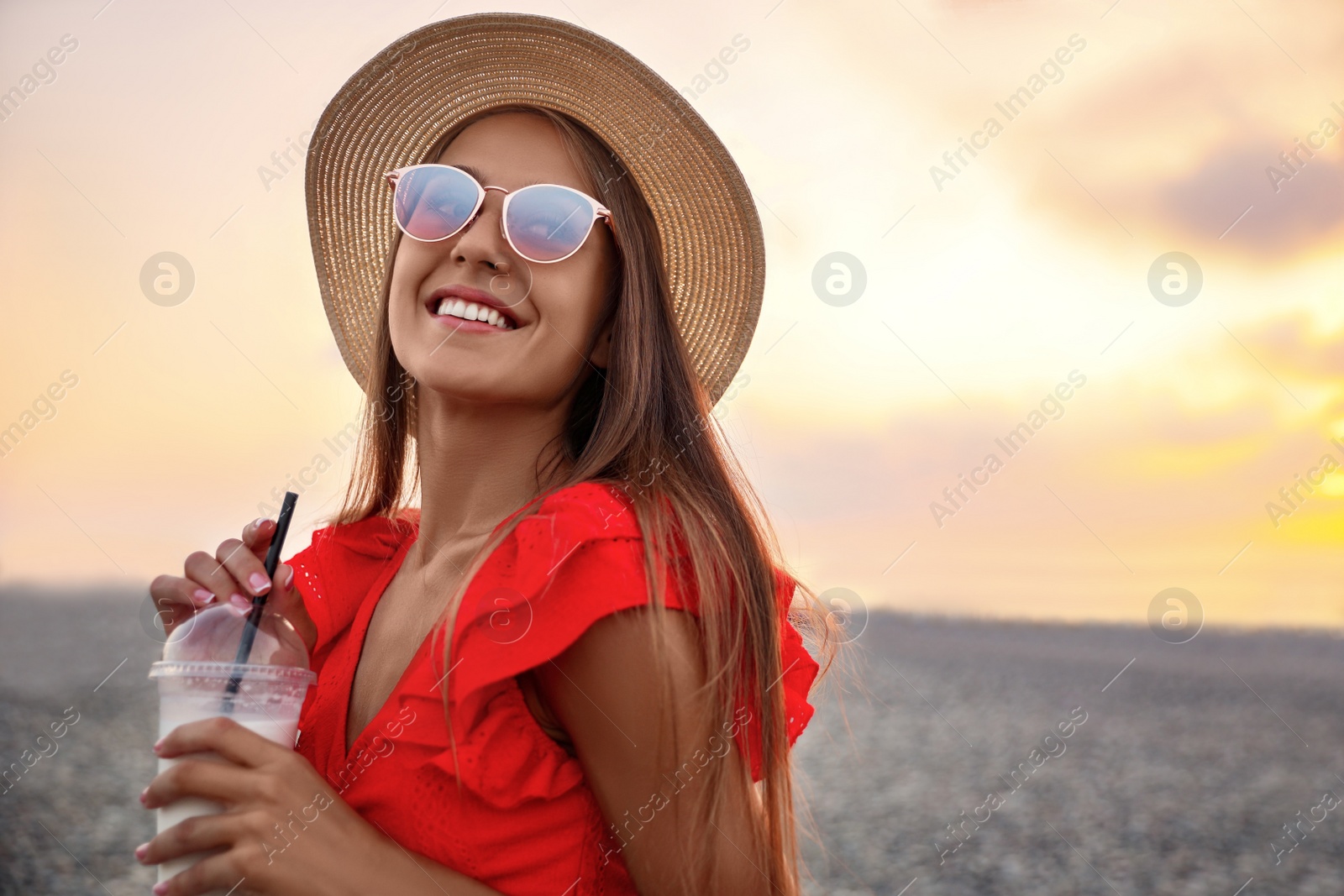 Photo of Beautiful young woman with tasty milk shake on beach, space for text