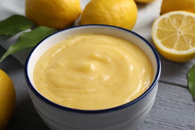 Photo of Delicious lemon curd in bowl, fresh citrus fruits and spoon on grey wooden table