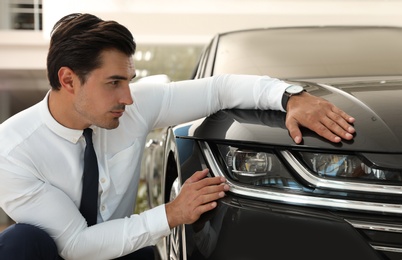 Young man checking new car in modern dealership