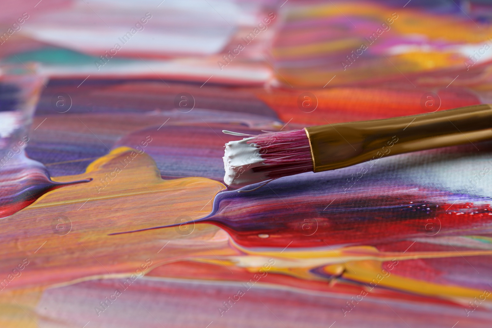 Photo of Brush on abstract colorful paint, closeup view