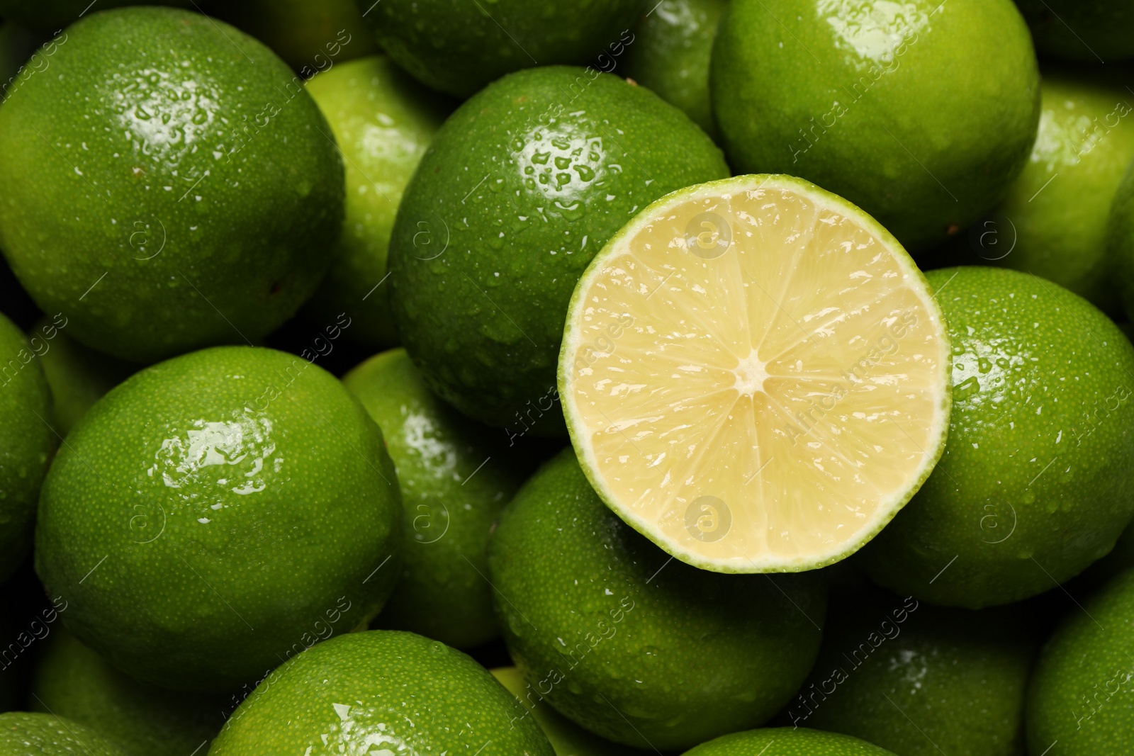 Photo of Whole and cut fresh limes with water drops as background, top view