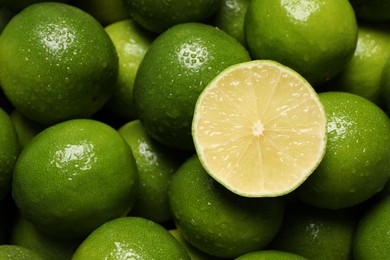 Photo of Whole and cut fresh limes with water drops as background, top view