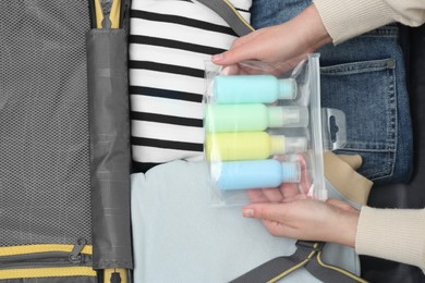 Photo of Woman with plastic bag of cosmetic travel kit packing suitcase, top view. Bath accessories