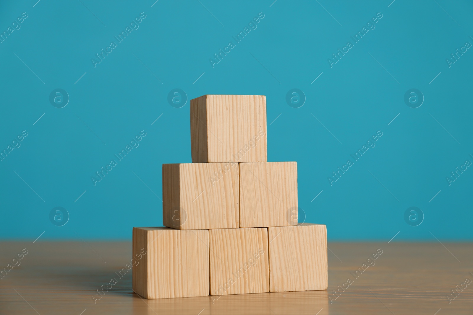 Photo of Pyramid of blank cubes on wooden table against light blue background. Space for text