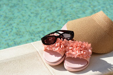 Photo of Stylish visor cap, slippers and sunglasses near outdoor swimming pool on sunny day, closeup. Space for text