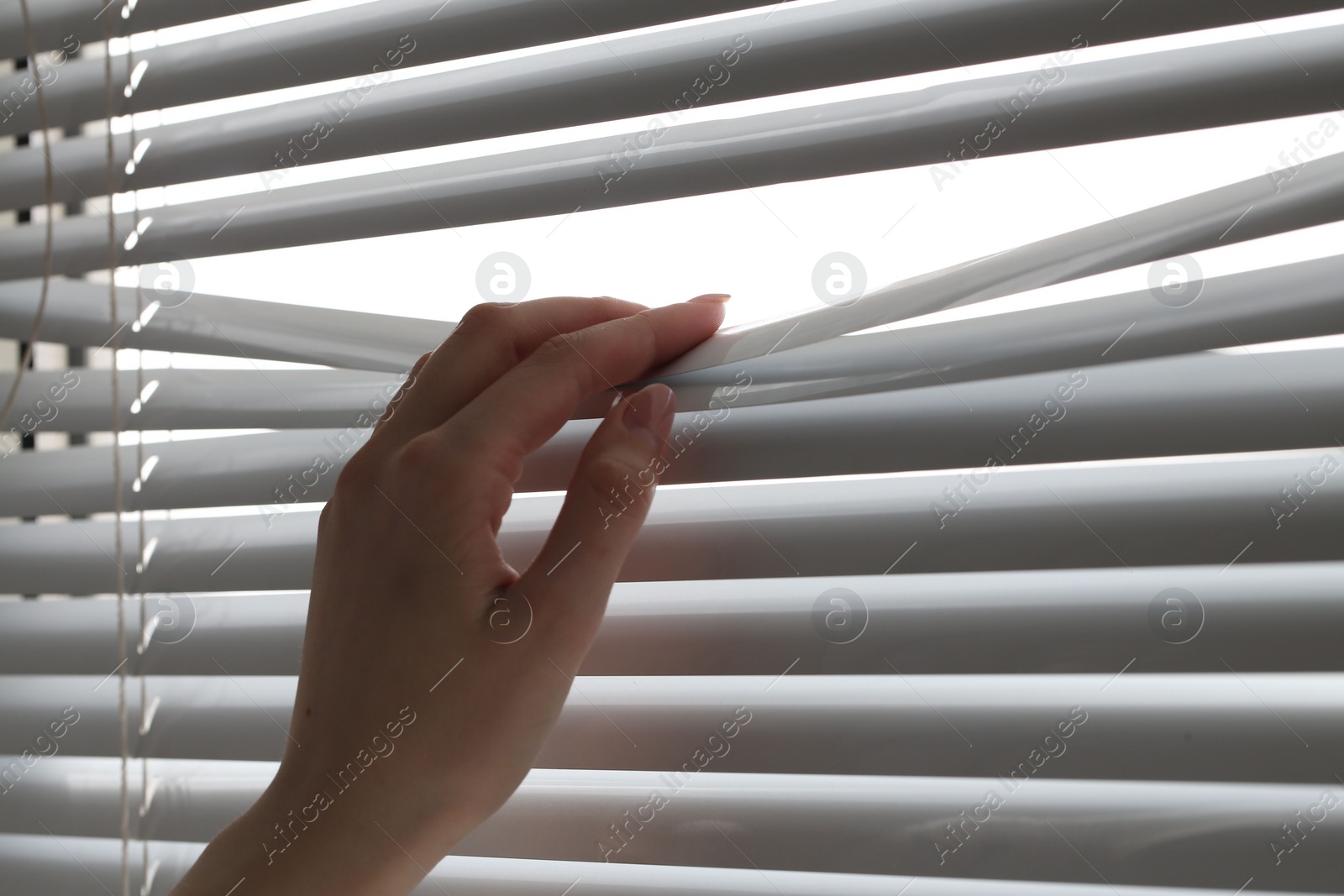 Photo of Woman separating slats of white blinds indoors, closeup