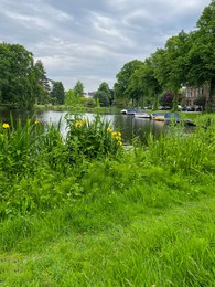 Beautiful view of city canal with moored boats surrounded by greenery on cloudy day