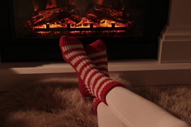 Woman in warm socks resting near fireplace with burning woods indoors, closeup