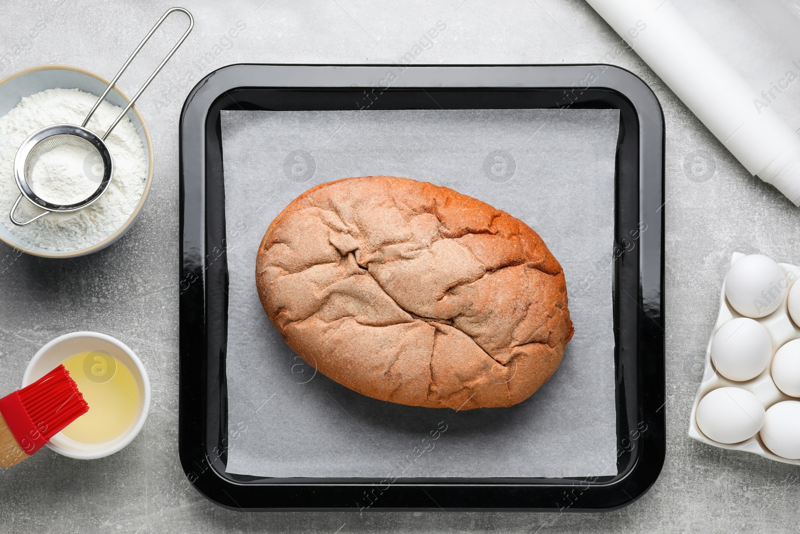 Photo of Parchment paper, baking pan with tasty homemade bread and different ingredients on light grey table, flat lay