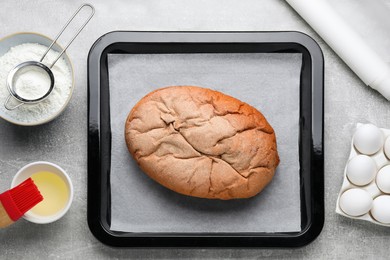 Parchment paper, baking pan with tasty homemade bread and different ingredients on light grey table, flat lay