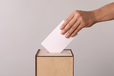 Man putting his vote into ballot box on light grey background, closeup