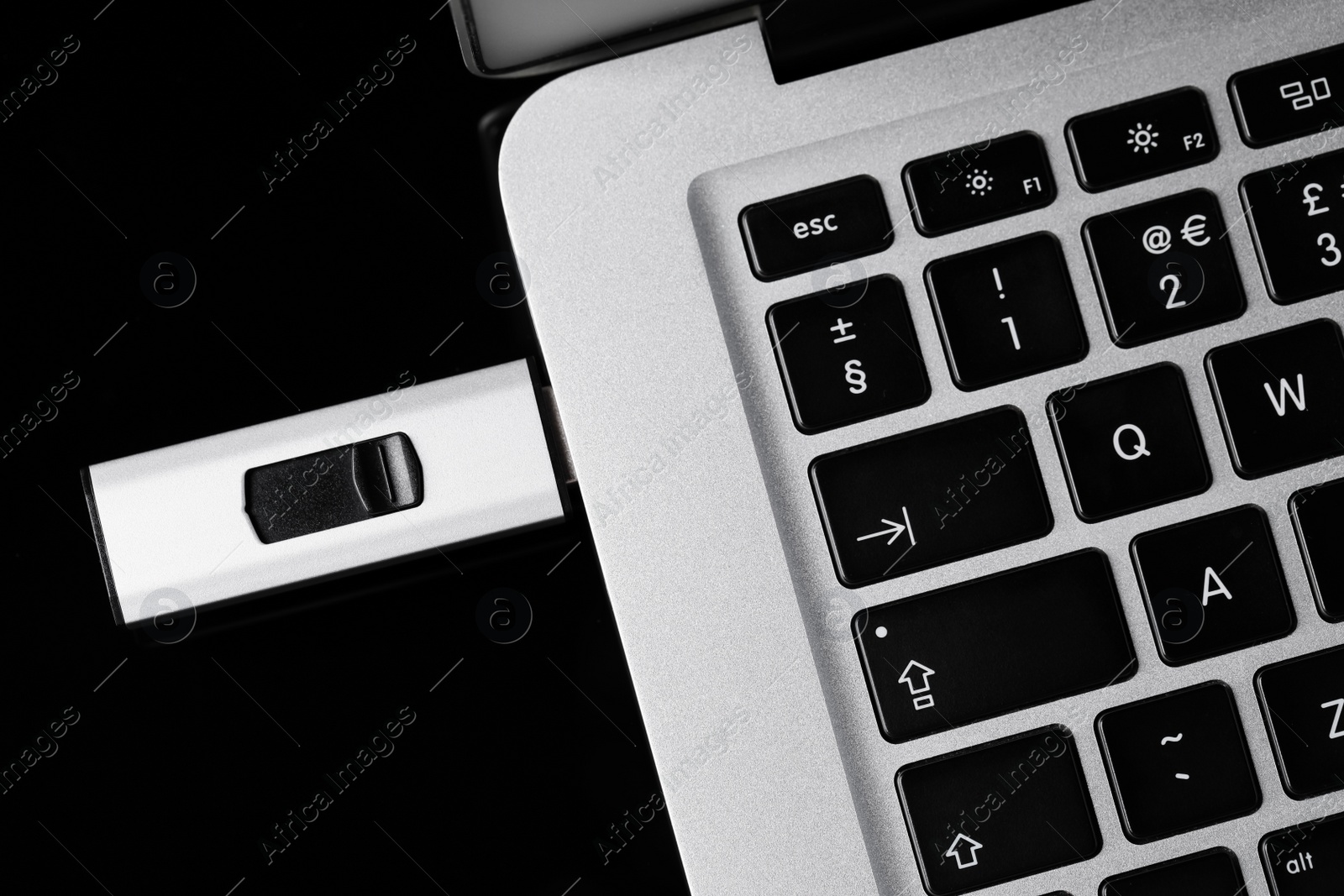 Photo of Modern usb flash drive attached into laptop on black table, top view