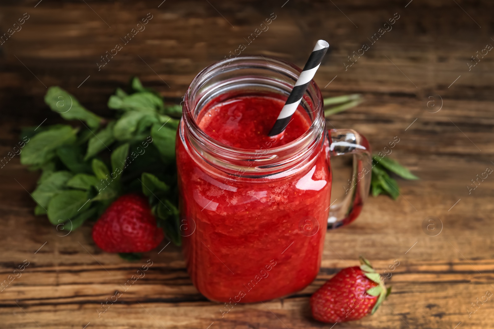 Photo of Tasty strawberry smoothie in mason jar on wooden table