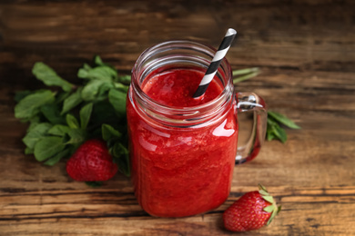 Photo of Tasty strawberry smoothie in mason jar on wooden table