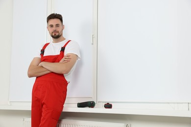 Worker in uniform near roller blinds on window indoors