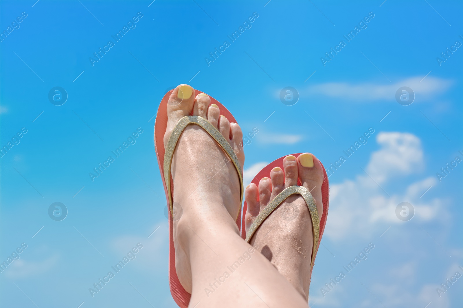 Photo of Woman in stylish pink flip flops against blue sky, closeup of feet