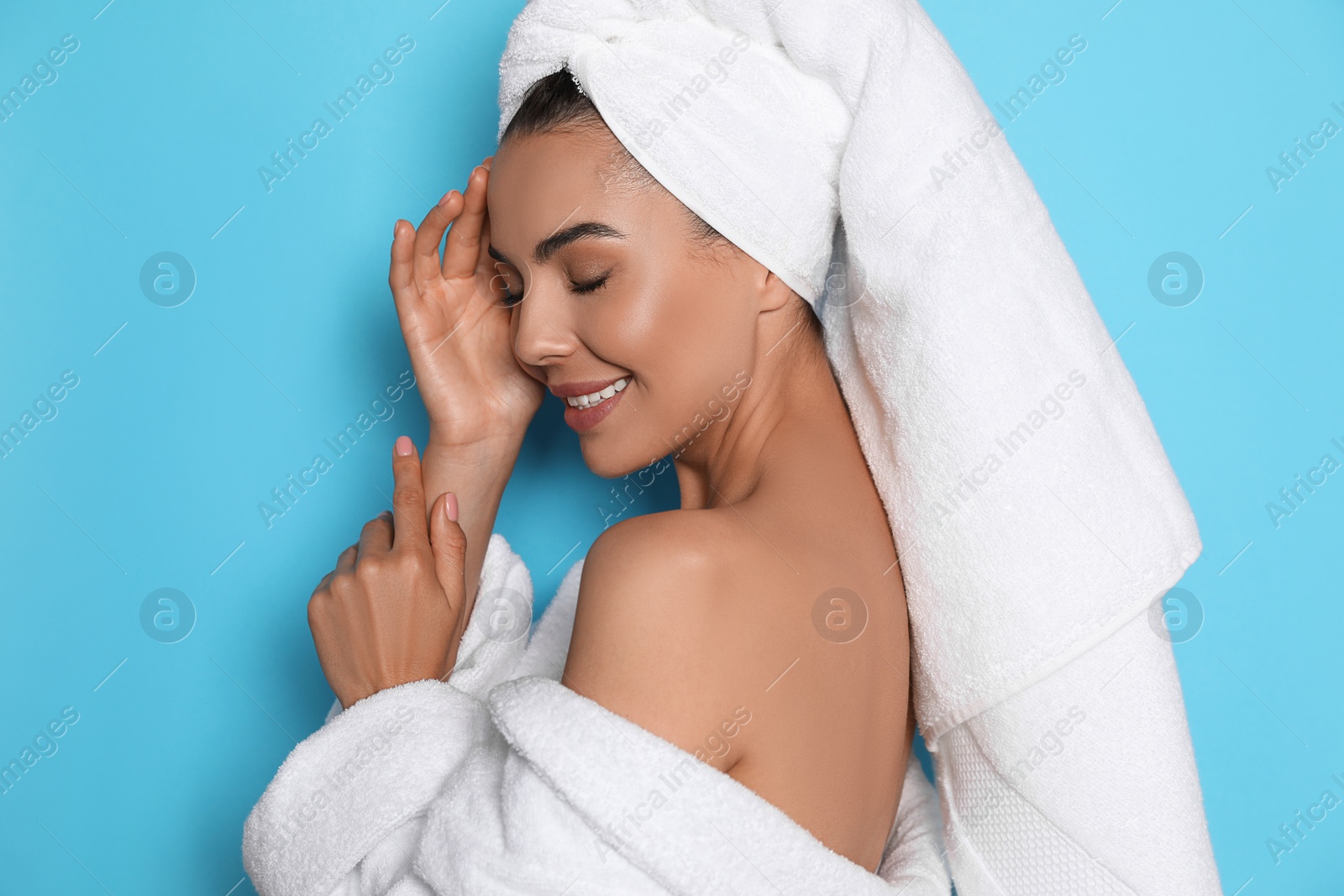 Photo of Beautiful young woman wearing bathrobe and towel on head against light blue background