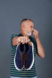 Man feeling bad smell from shoes on color background. Air freshener