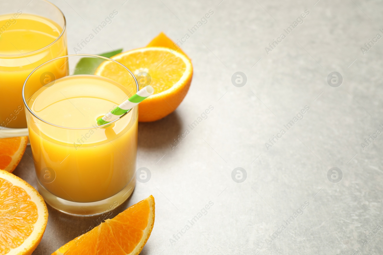 Photo of Glasses of orange juice and fresh fruits on light grey table, closeup. Space for text