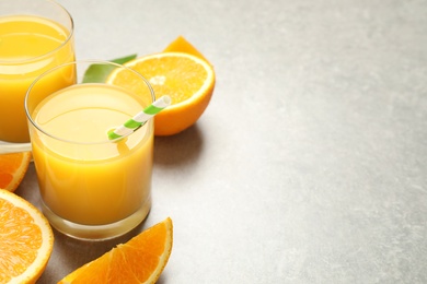 Photo of Glasses of orange juice and fresh fruits on light grey table, closeup. Space for text