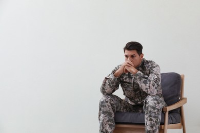 Stressed military officer sitting in armchair near white wall indoors. Space for text