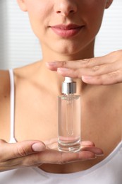 Woman with bottle of cosmetic serum on light background, closeup