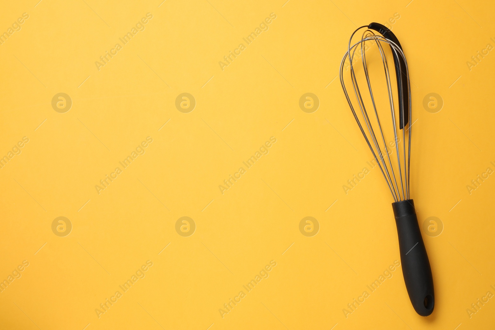 Photo of Metal whisk on yellow background, top view. Space for text