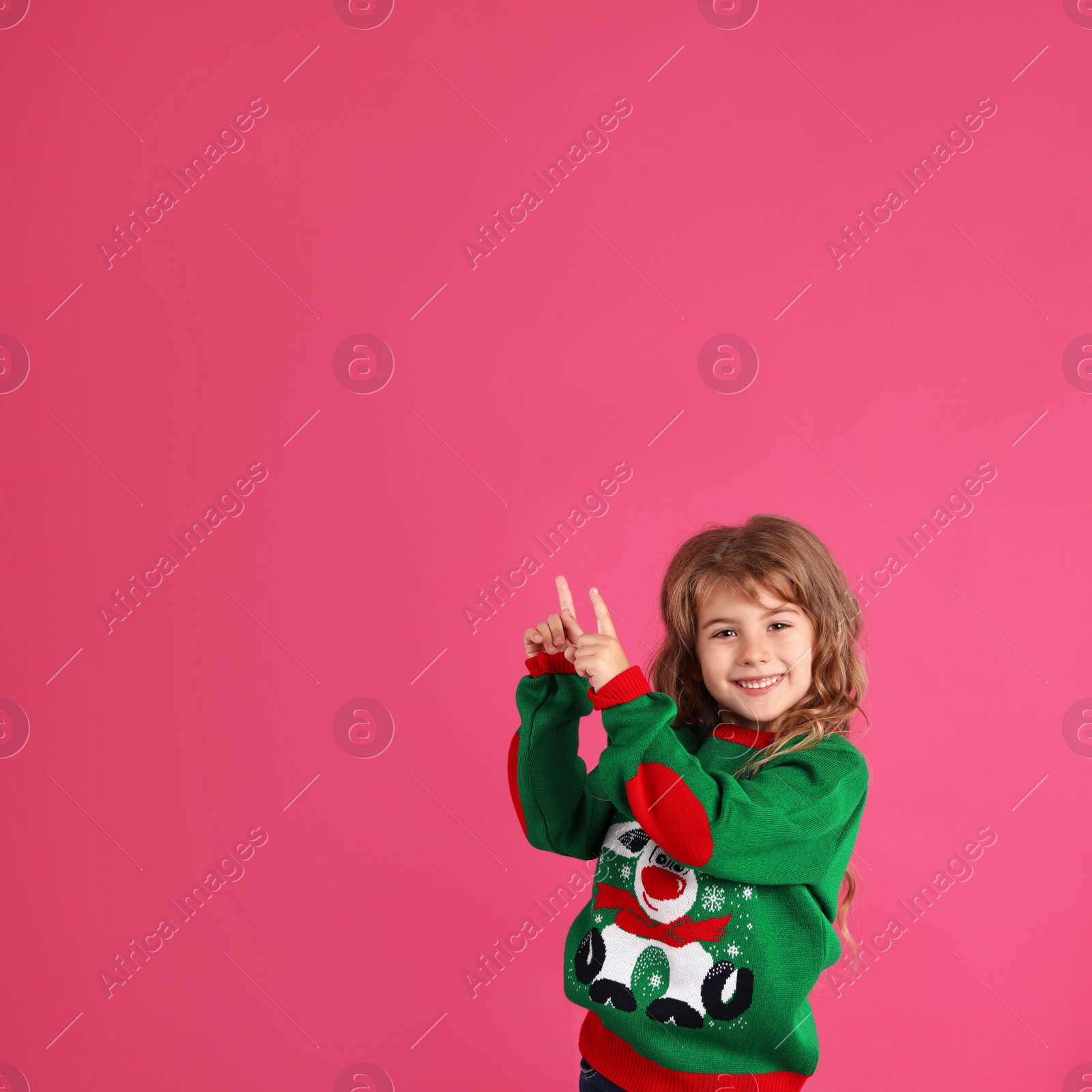 Photo of Cute little girl in green Christmas sweater pointing against pink background. Space for text