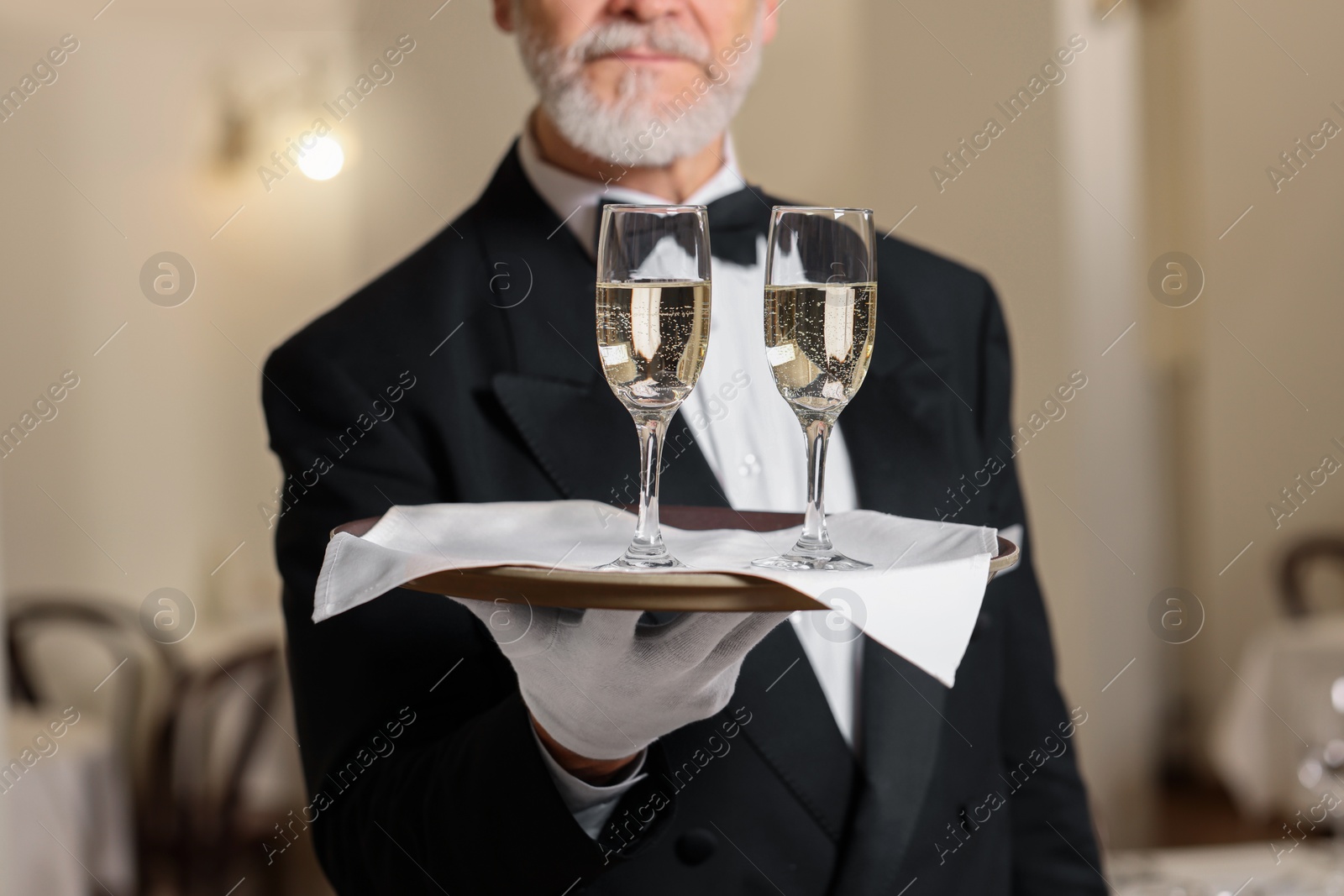 Photo of Senior butler holding tray with glasses of sparkling wine in restaurant, closeup